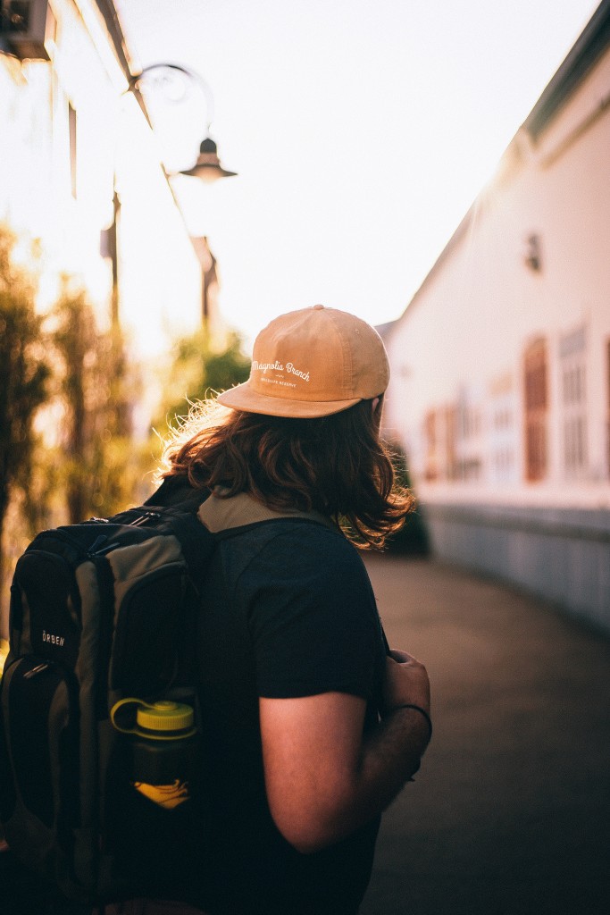 A long-haired man with a backpack on is wearing an orange hat with 